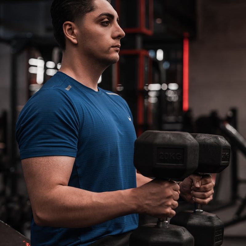 Man focused on lifting a dumbbell with proper form in a minimalist gym.